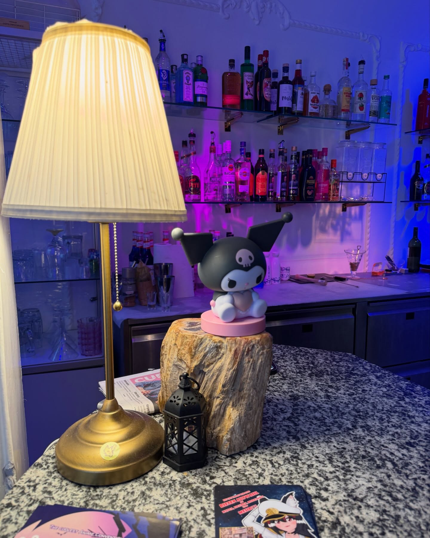 Die Akira-Bar mit warmer Tischlampe, Kuromi-Figur und beleuchteten Flaschenregalen